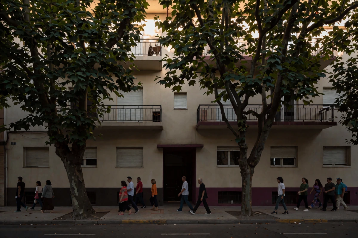Four people walk beside a residential facade with balconies, shutters, and trees